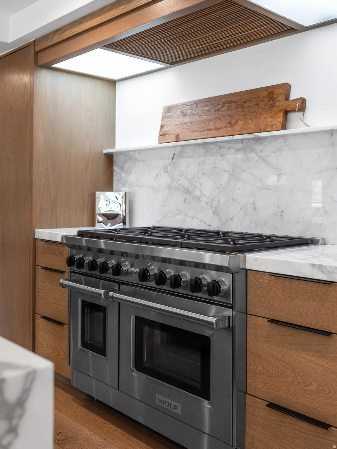 Professional-grade stainless steel range with double ovens, complemented by wood-finish cabinetry, a marble-clad backsplash, and a coordinating marble countertop