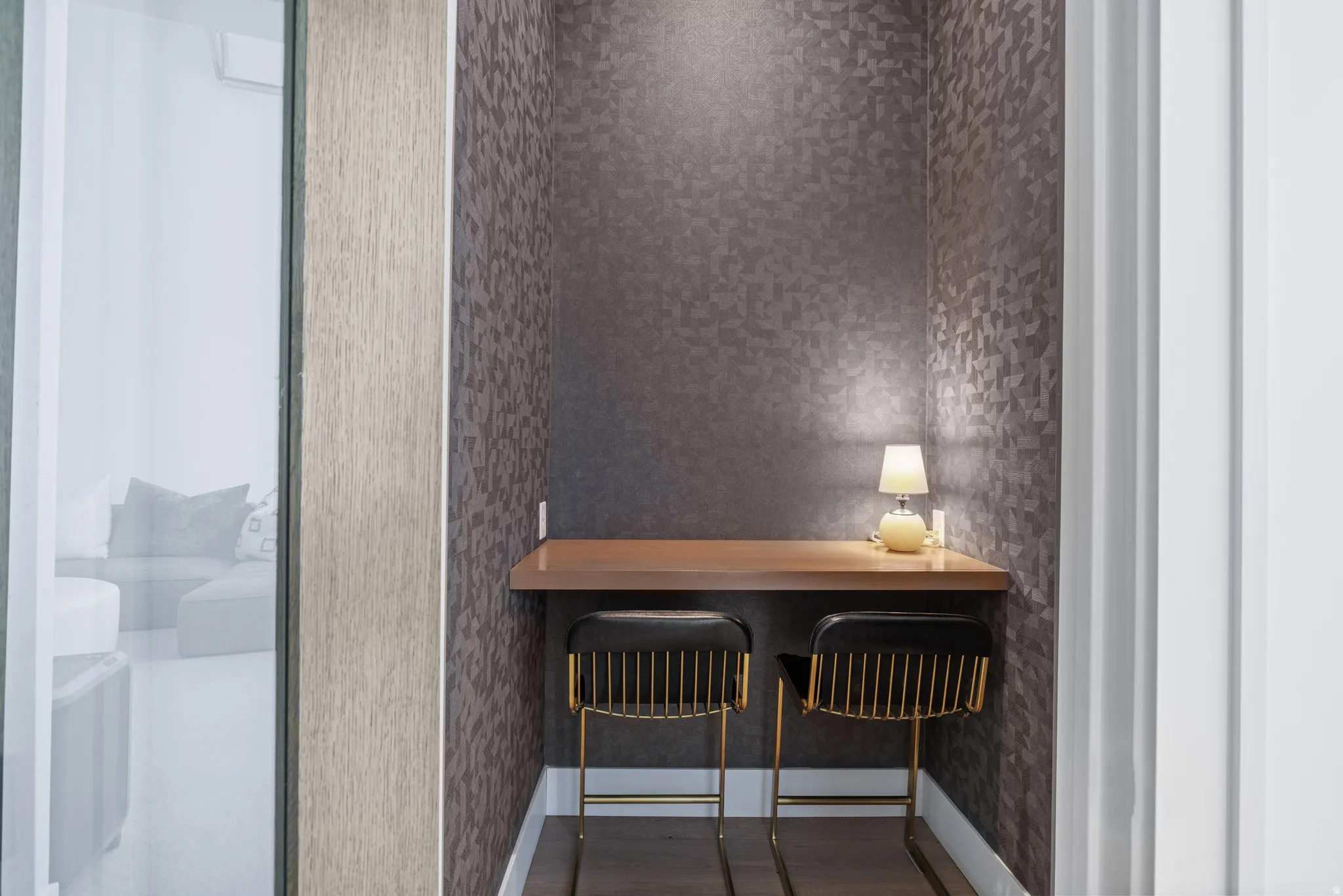 Built-in desk nook featuring a floating wood-finish surface, geometric pattern wallpaper, and dark wood-finish flooring