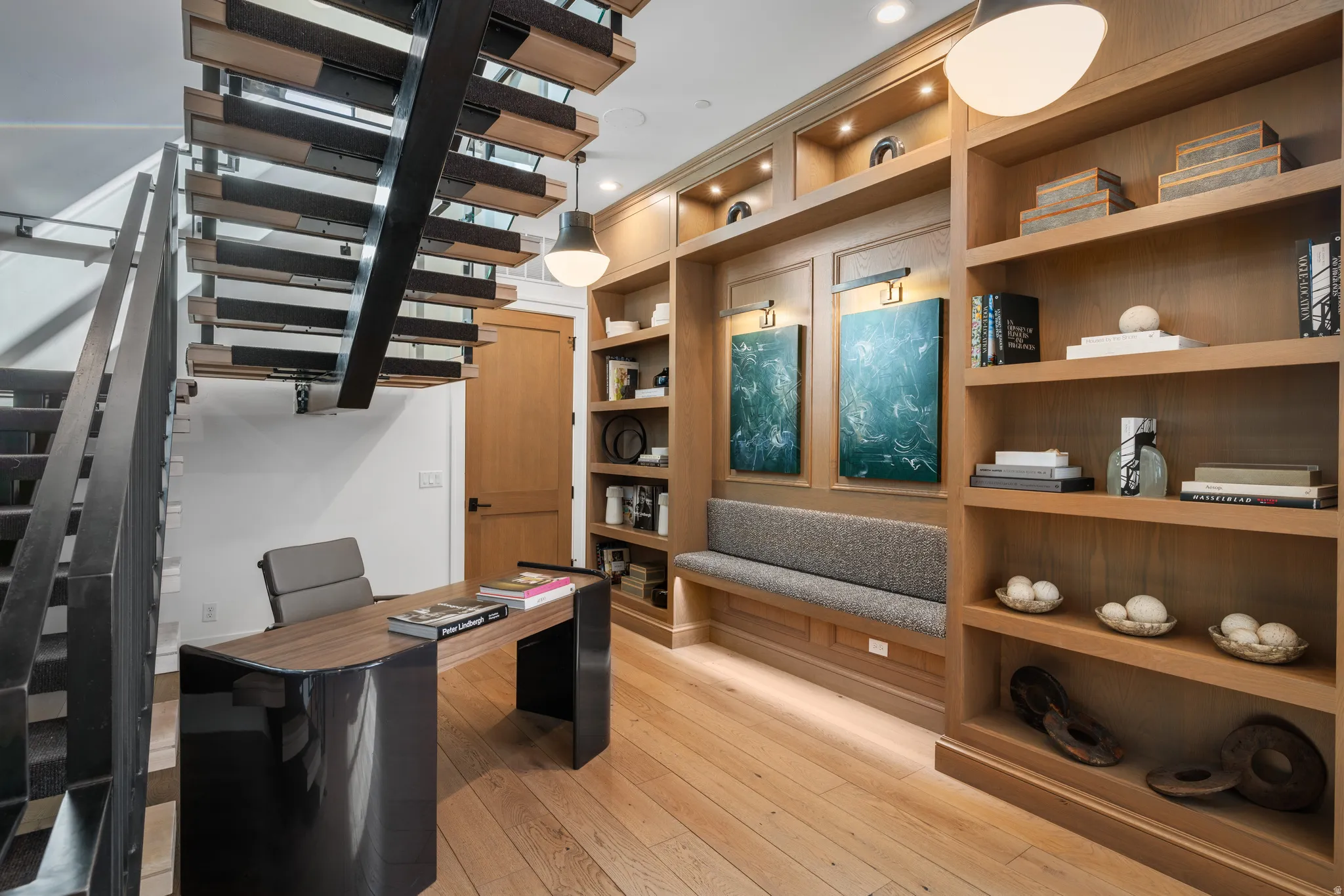 Custom built-in shelving with integrated lighting, wood-finish flooring, and a contemporary open-riser staircase with metal railings
