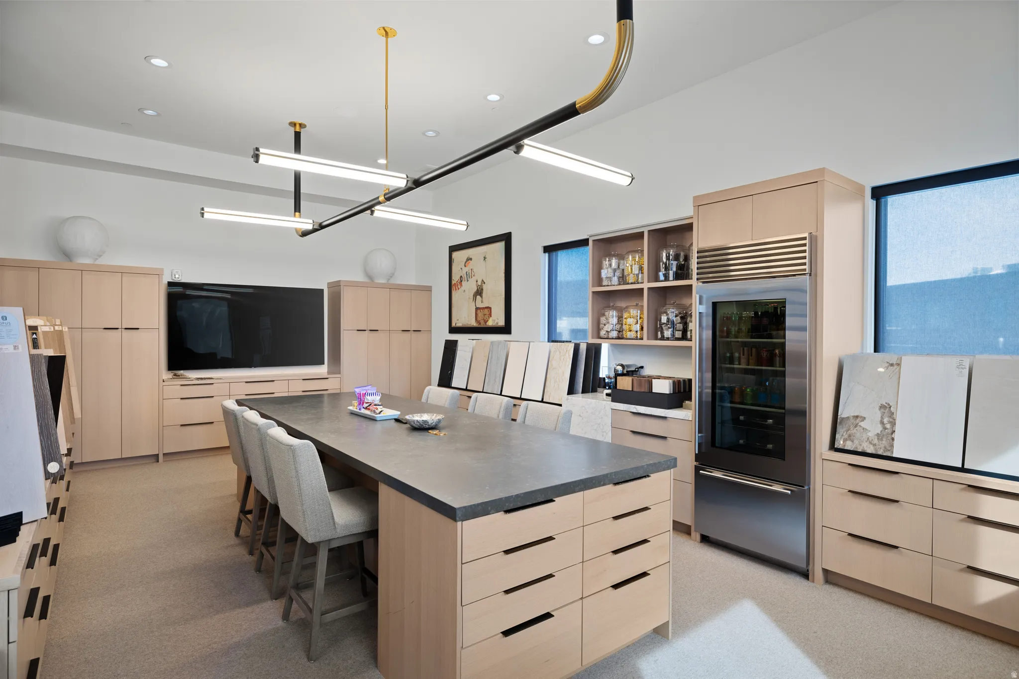 Expansive room featuring a large central island with seating, extensive light wood-finish cabinetry, built-in refrigeration, and contemporary linear light fixtures