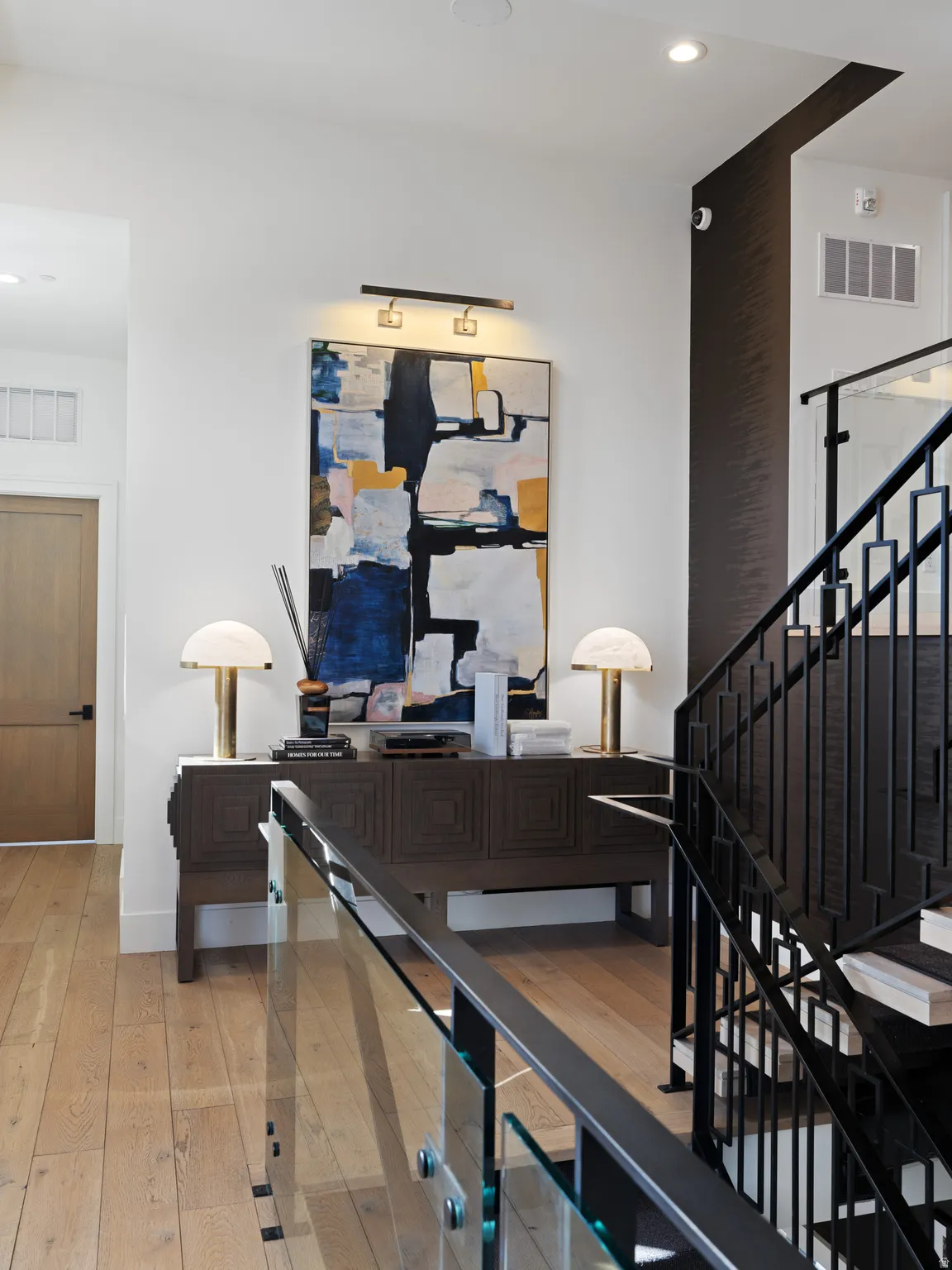 Entryway featuring wood-finish flooring, a dark wood console table, and a contemporary glass and metal staircase railing