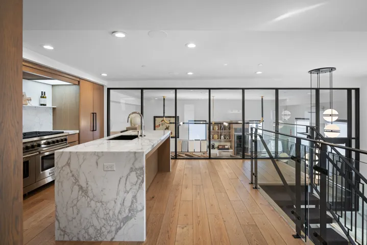 Open-concept kitchen featuring an oversized stone island with waterfall edges and an undermount sink