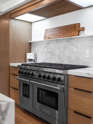 Professional-grade stainless steel range with double ovens, complemented by wood-finish cabinetry, a marble-clad backsplash, and a coordinating marble countertop