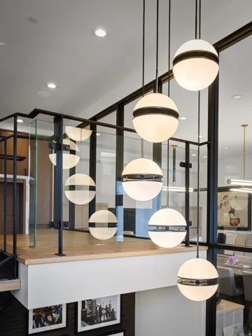 Modern spherical pendant lights illuminate a landing featuring a glass and black metal railing system