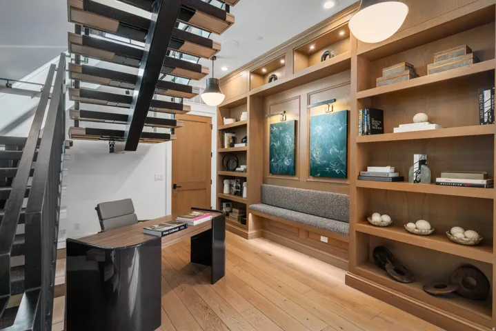 Custom built-in shelving with integrated lighting, wood-finish flooring, and a contemporary open-riser staircase with metal railings