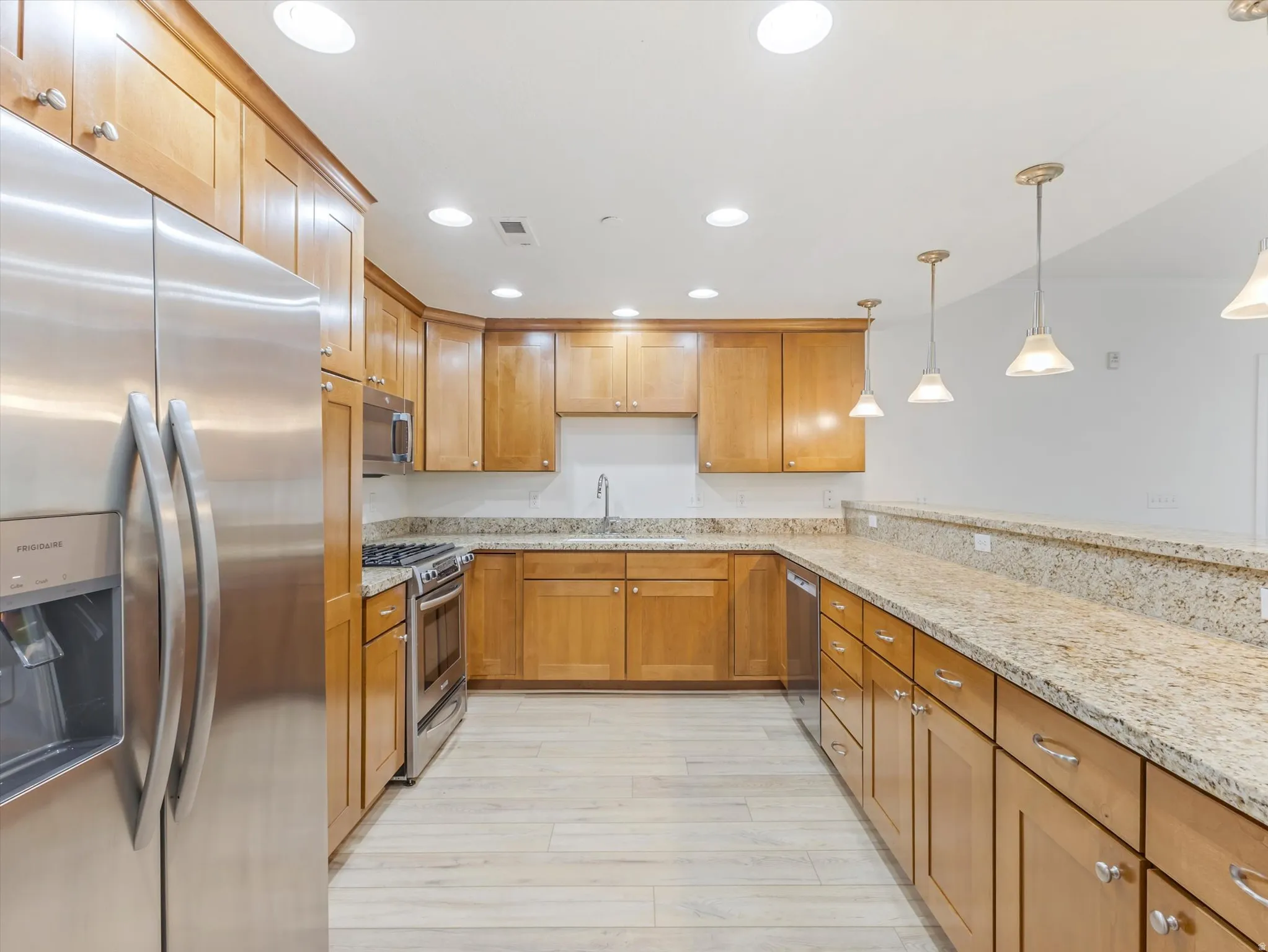 Open-concept kitchen featuring wood cabinetry, stainless steel appliances, and light-toned granite countertops