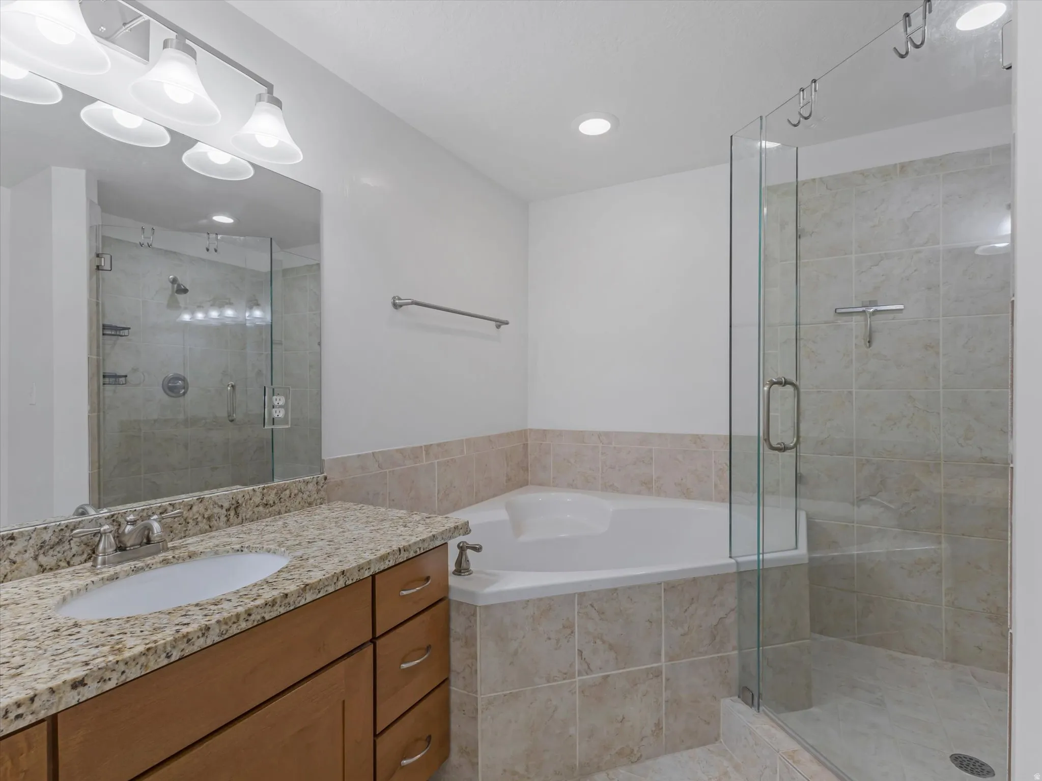 Bathroom featuring a corner soaking tub, glass-enclosed shower with tiled walls, and a vanity with a granite-style countertop