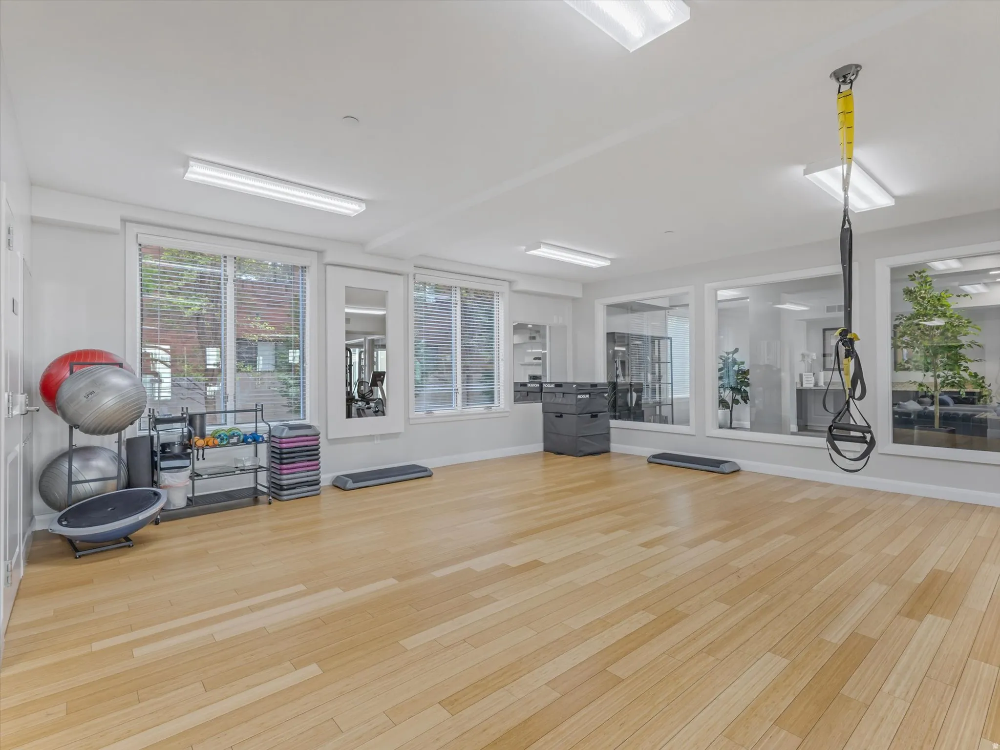 Spacious fitness area featuring light wood-finish flooring, recessed lighting, and multiple windows with blinds