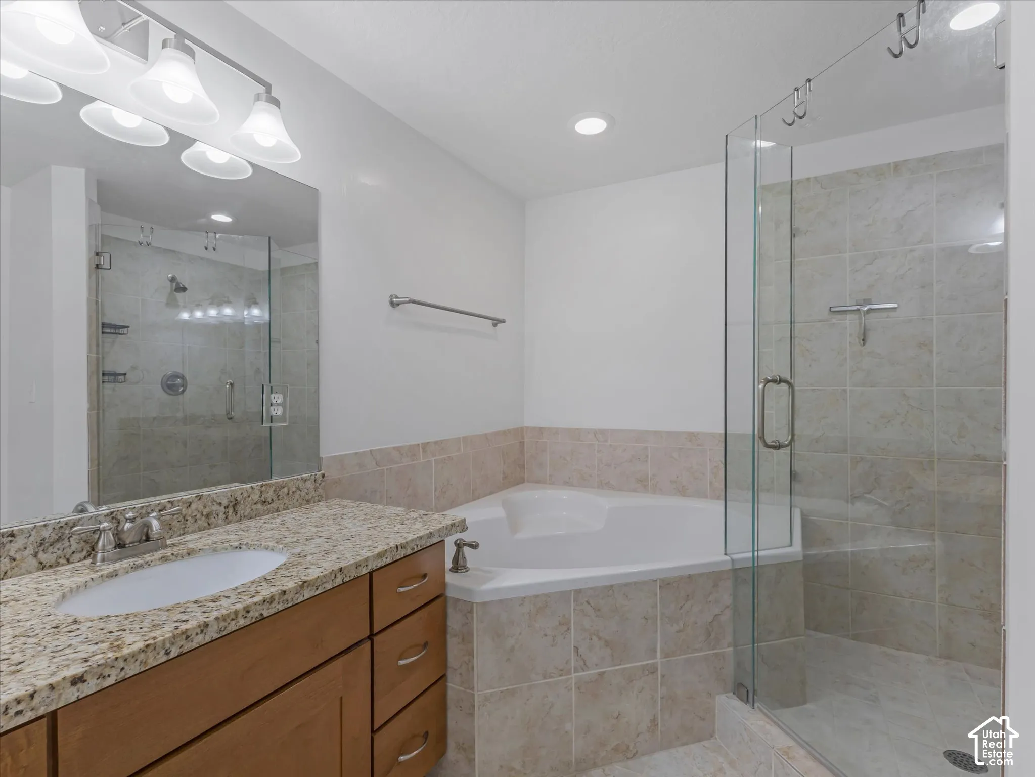 Bathroom featuring a corner soaking tub, glass-enclosed shower with tiled walls, and a vanity with a granite-style countertop