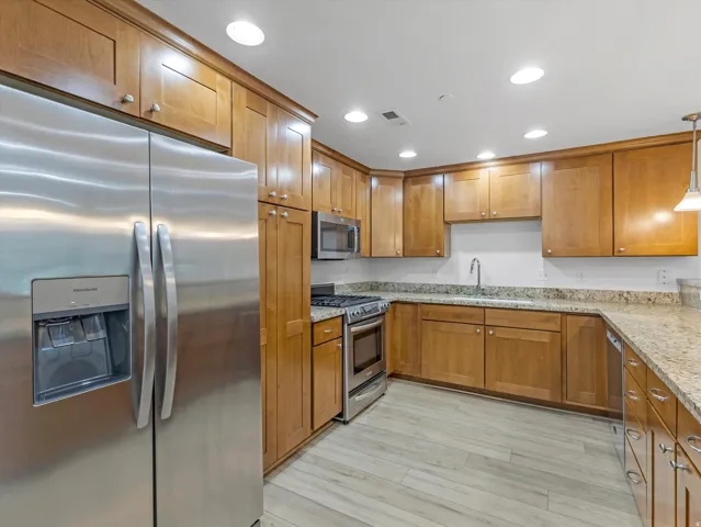 Kitchen featuring stainless steel appliances, wood-finish cabinetry, stone countertops, and wood-look flooring