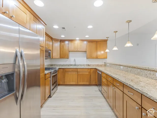 Open-concept kitchen featuring wood cabinetry, stainless steel appliances, and light-toned granite countertops