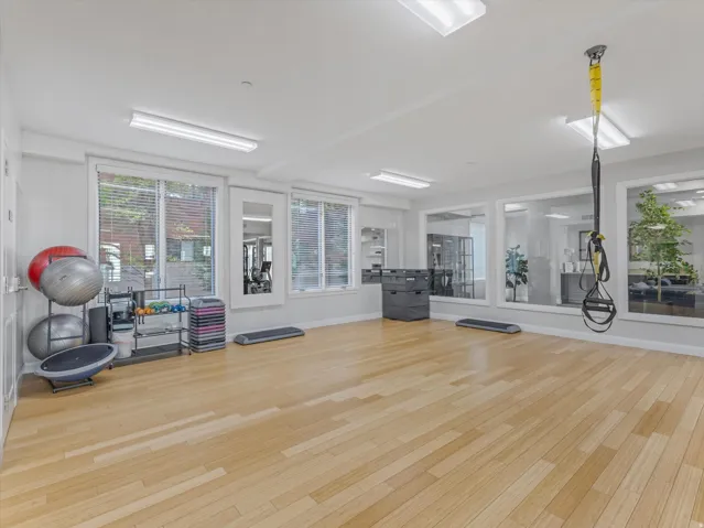 Spacious fitness area featuring light wood-finish flooring, recessed lighting, and multiple windows with blinds