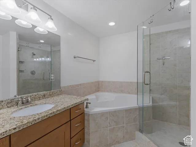 Bathroom featuring a corner soaking tub, glass-enclosed shower with tiled walls, and a vanity with a granite-style countertop