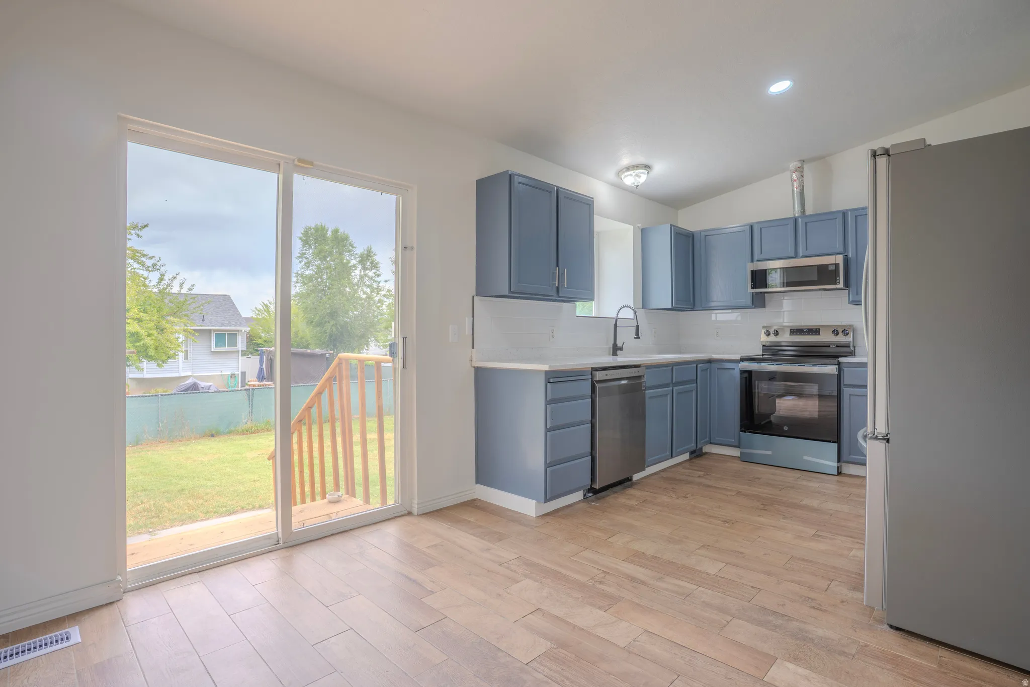 Kitchen featuring blue cabinetry, stainless steel appliances, white subway tile backsplash, and light wood-finish flooring