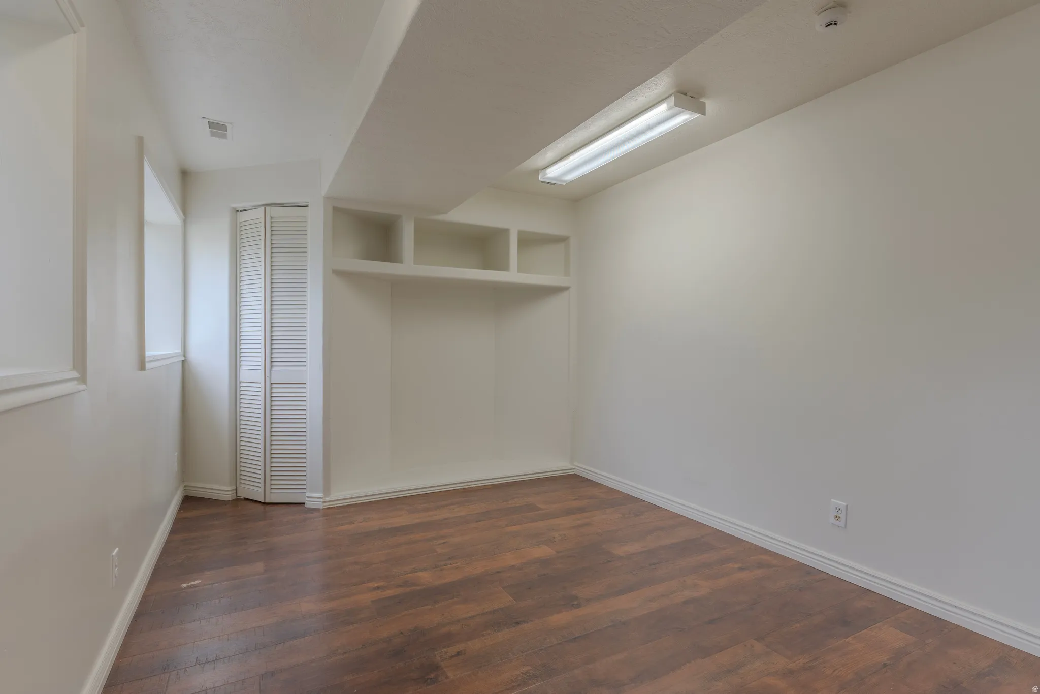 Room featuring wood-finish flooring, built-in shelving, a bi-fold louvered closet door, and a recessed window