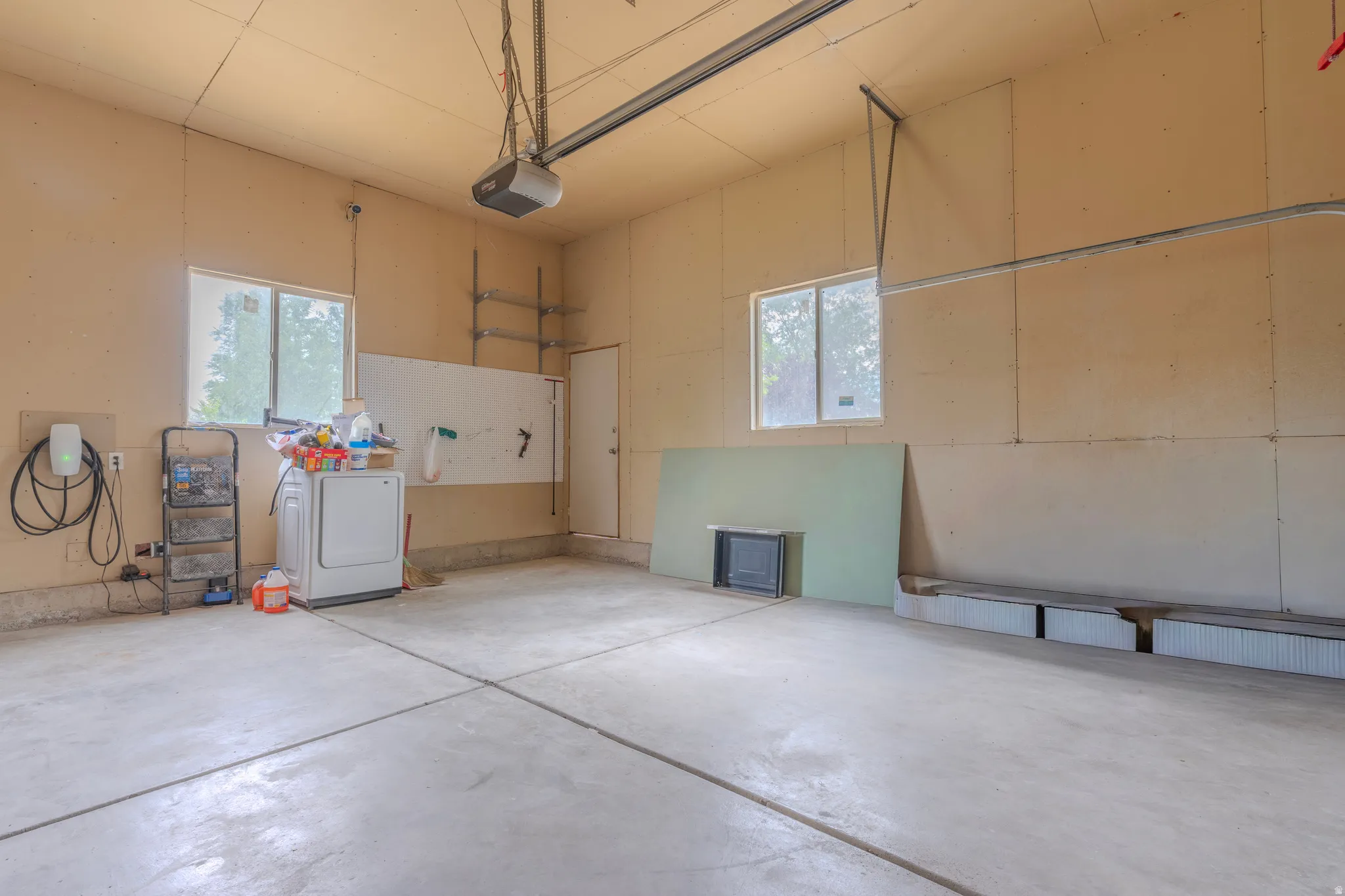 Spacious garage featuring concrete flooring, two window openings, an overhead door opener, a wall-mounted EV charging station, and an interior access door