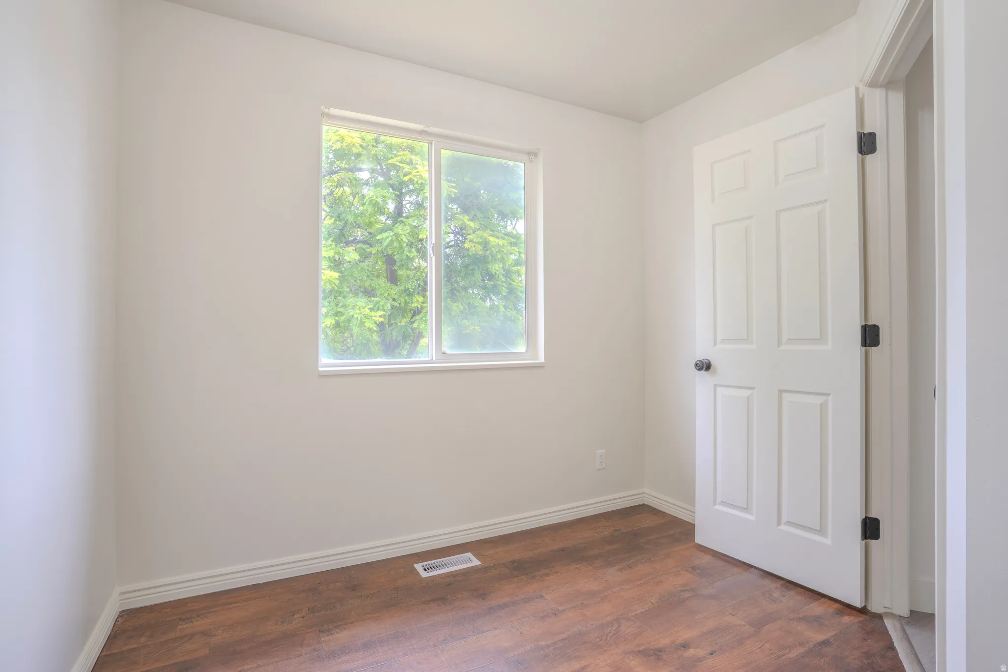 Bright room featuring a large window, wood-finish flooring, white baseboards, a paneled door, and neutral wall paint