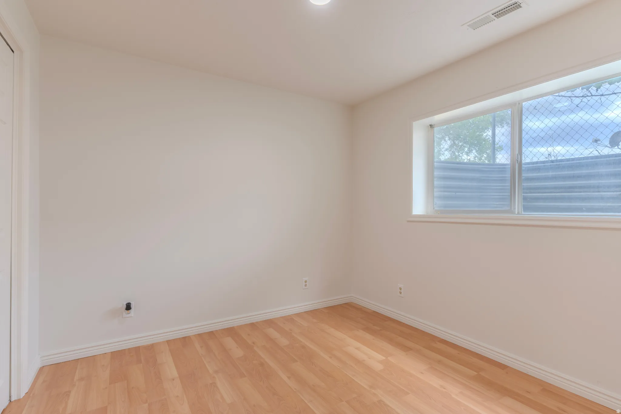 Room featuring wood-finish flooring, white baseboards, a white door, a window with a security screen, and a recessed ceiling light