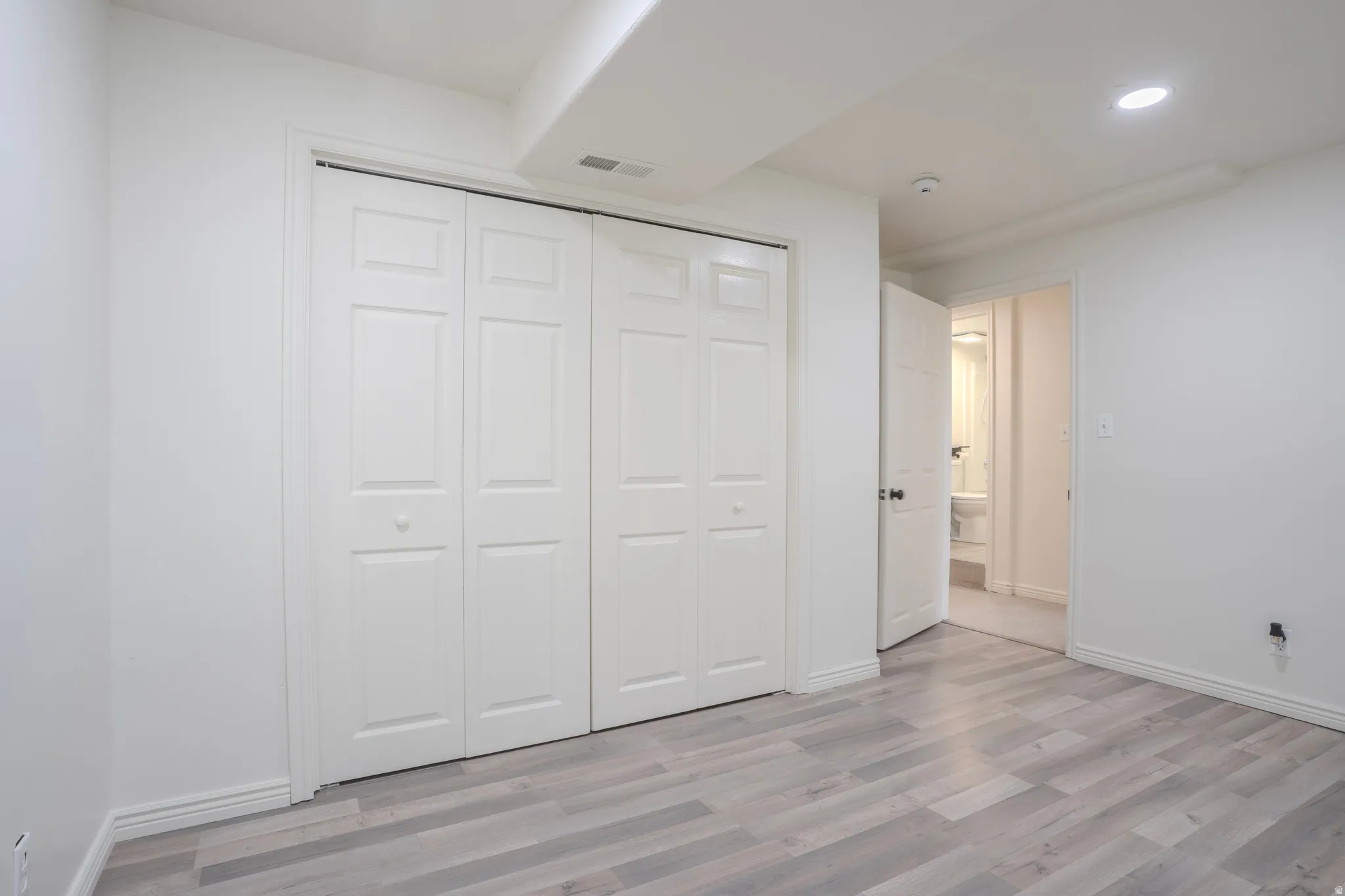 Room featuring light-toned wood-finish flooring, white baseboards, and a series of white bi-fold closet doors