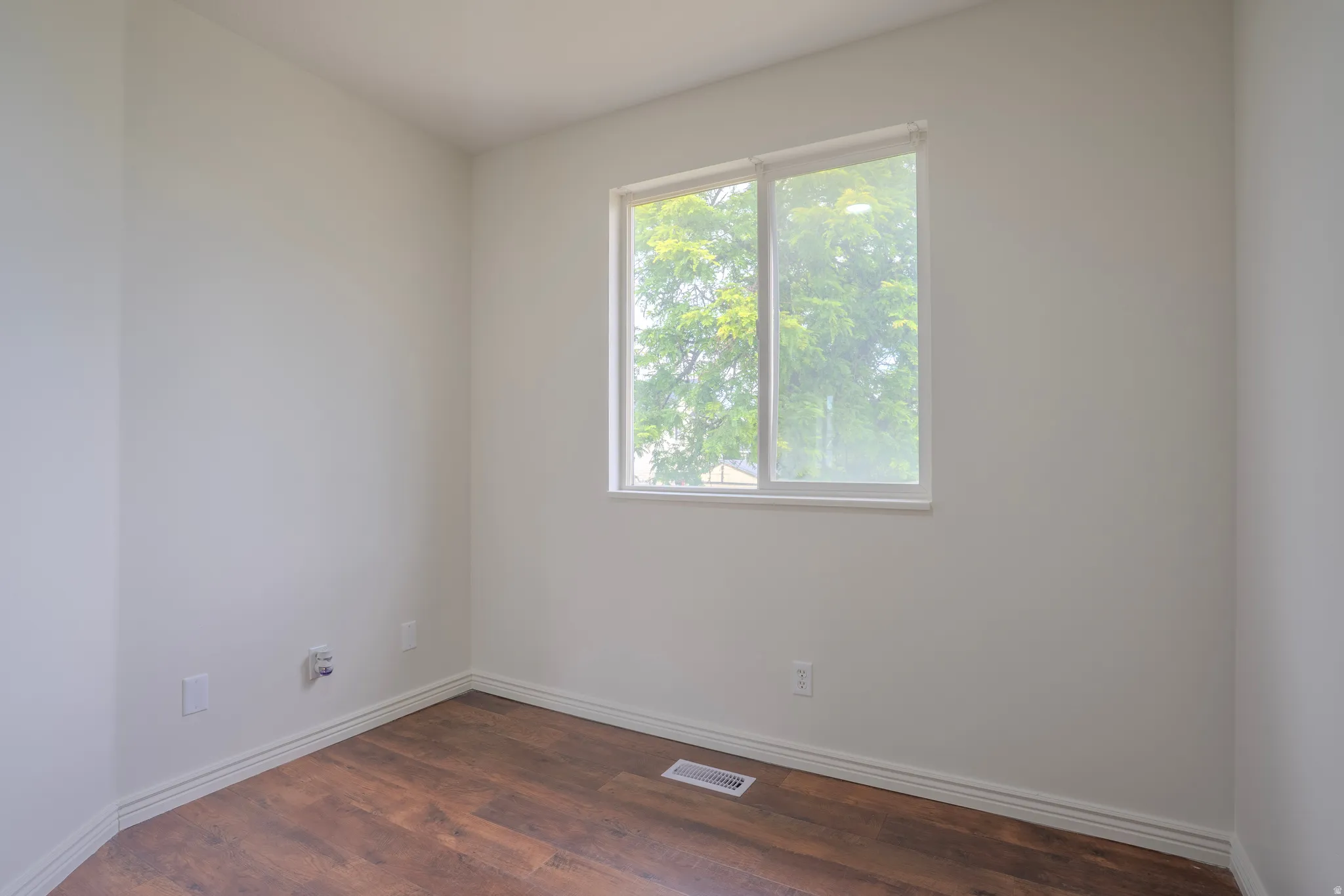 Bright interior space with a window, wood-finish flooring, white baseboards, and neutral wall paint