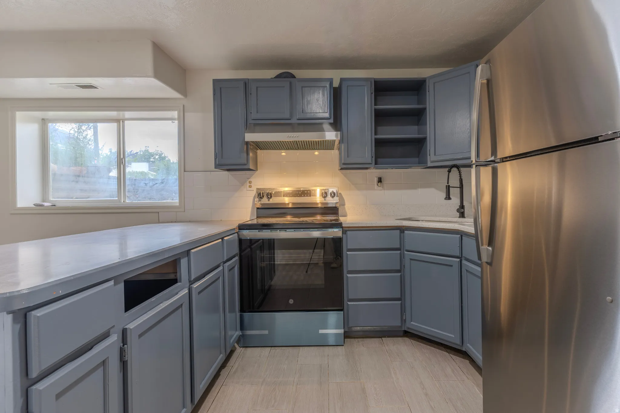 U-shaped kitchen featuring slate gray cabinetry, stainless steel appliances, white subway tile backsplash, and light-toned wood-finish flooring