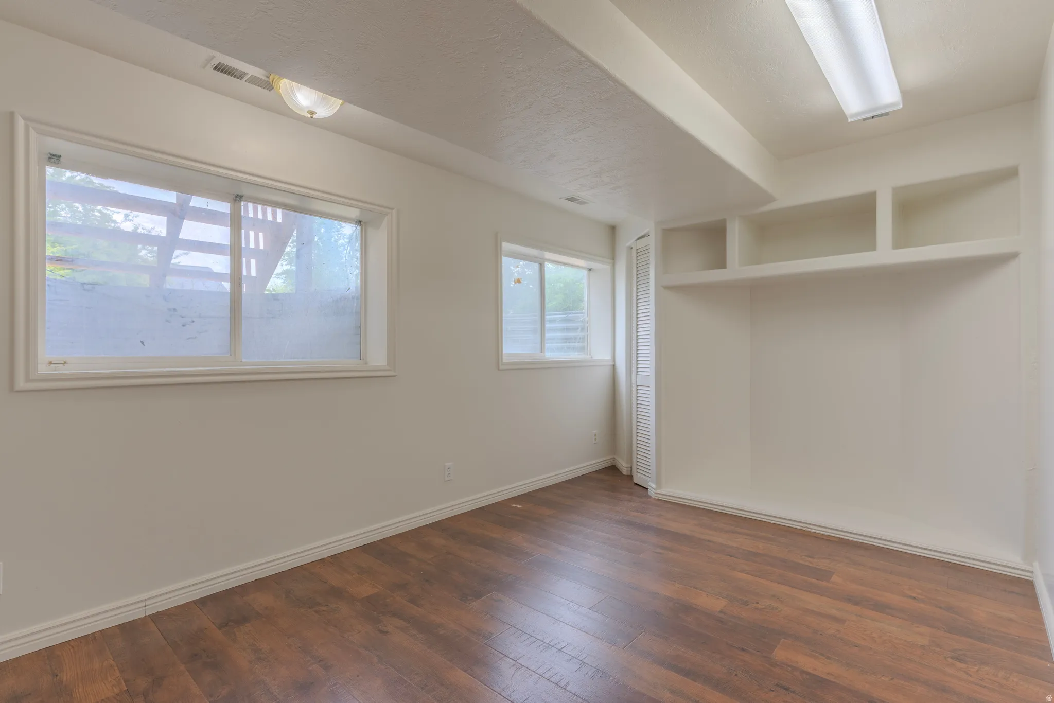 Room featuring wood-finish flooring, white walls, and built-in shelving