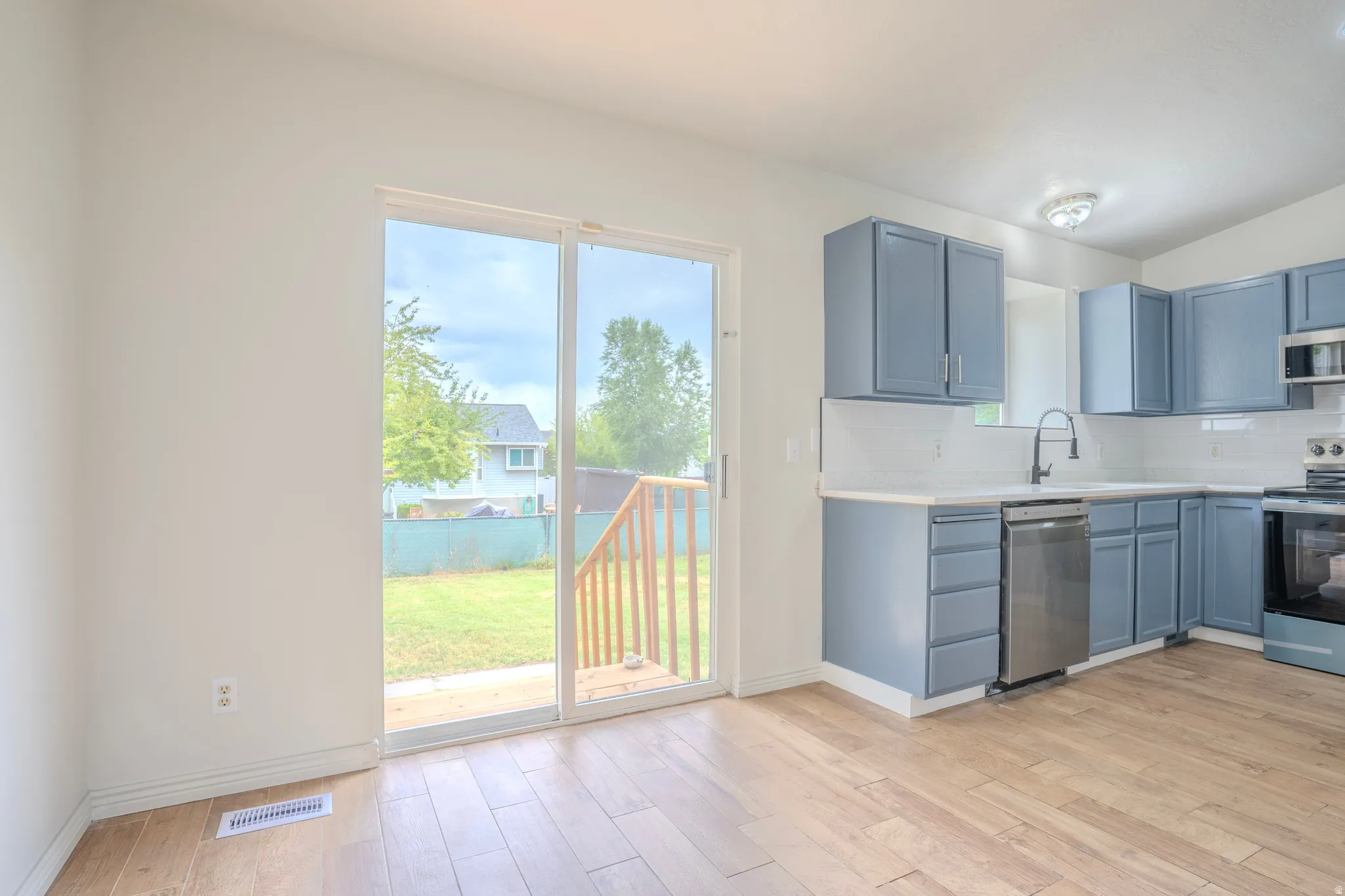 Kitchen featuring light blue cabinetry, stainless steel appliances, white subway tile backsplash, and wood-finish flooring