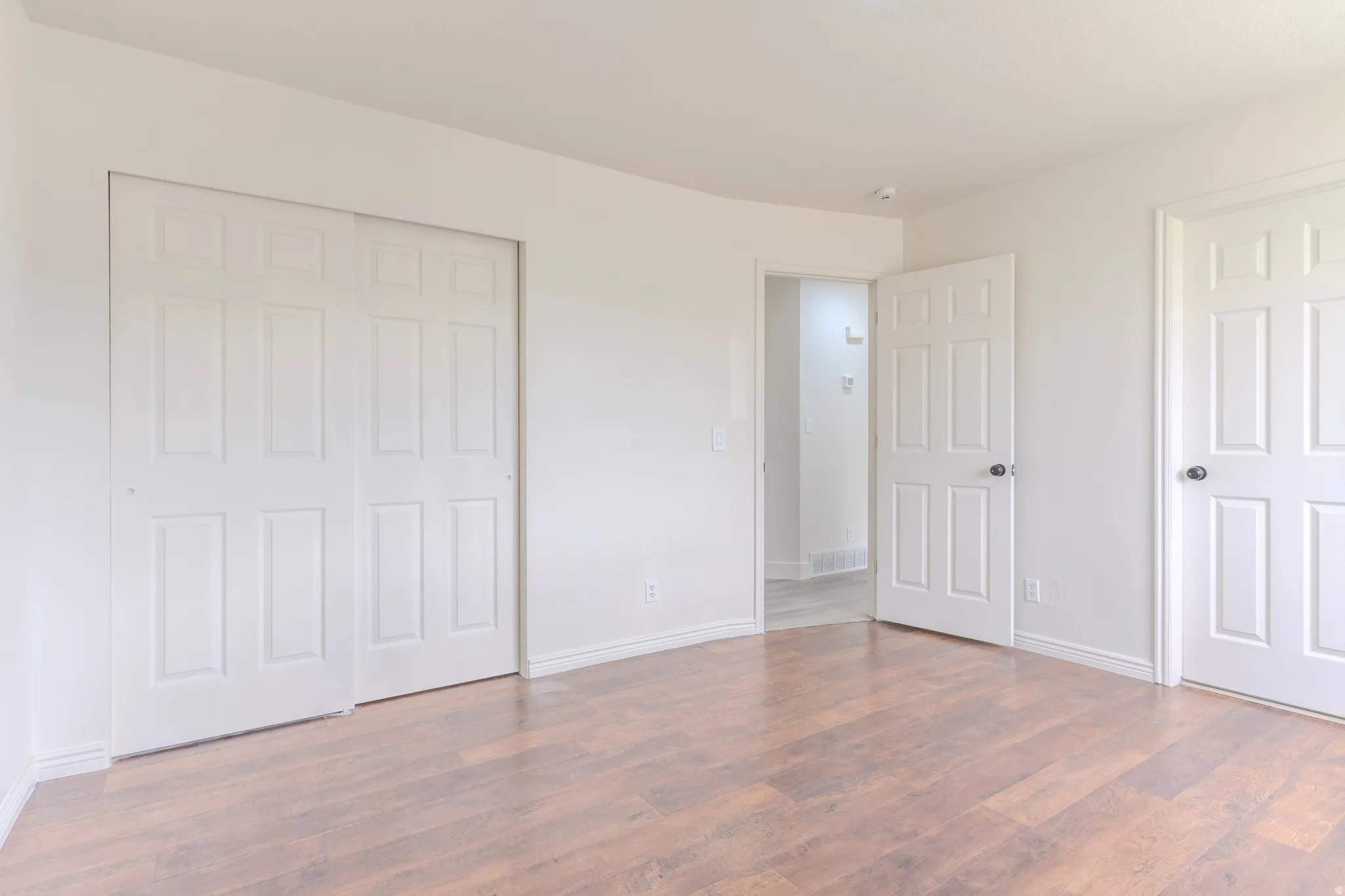 Spacious room featuring wood-finish flooring, white baseboards, and bright white walls