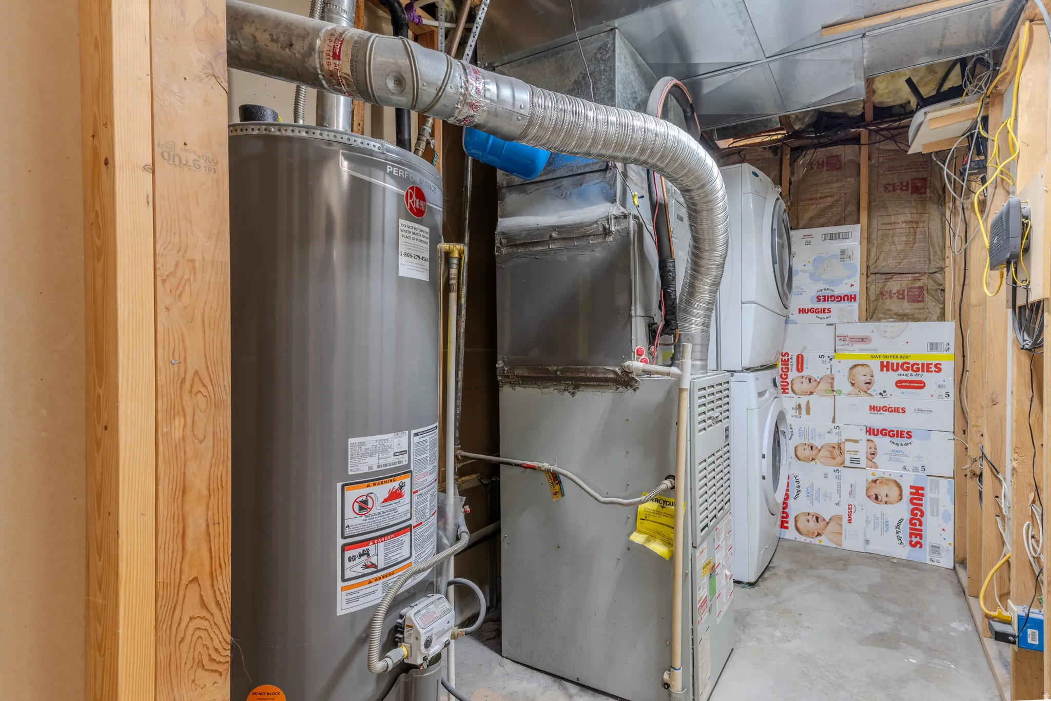 Utility area featuring a water heater, furnace, and stacked laundry appliances