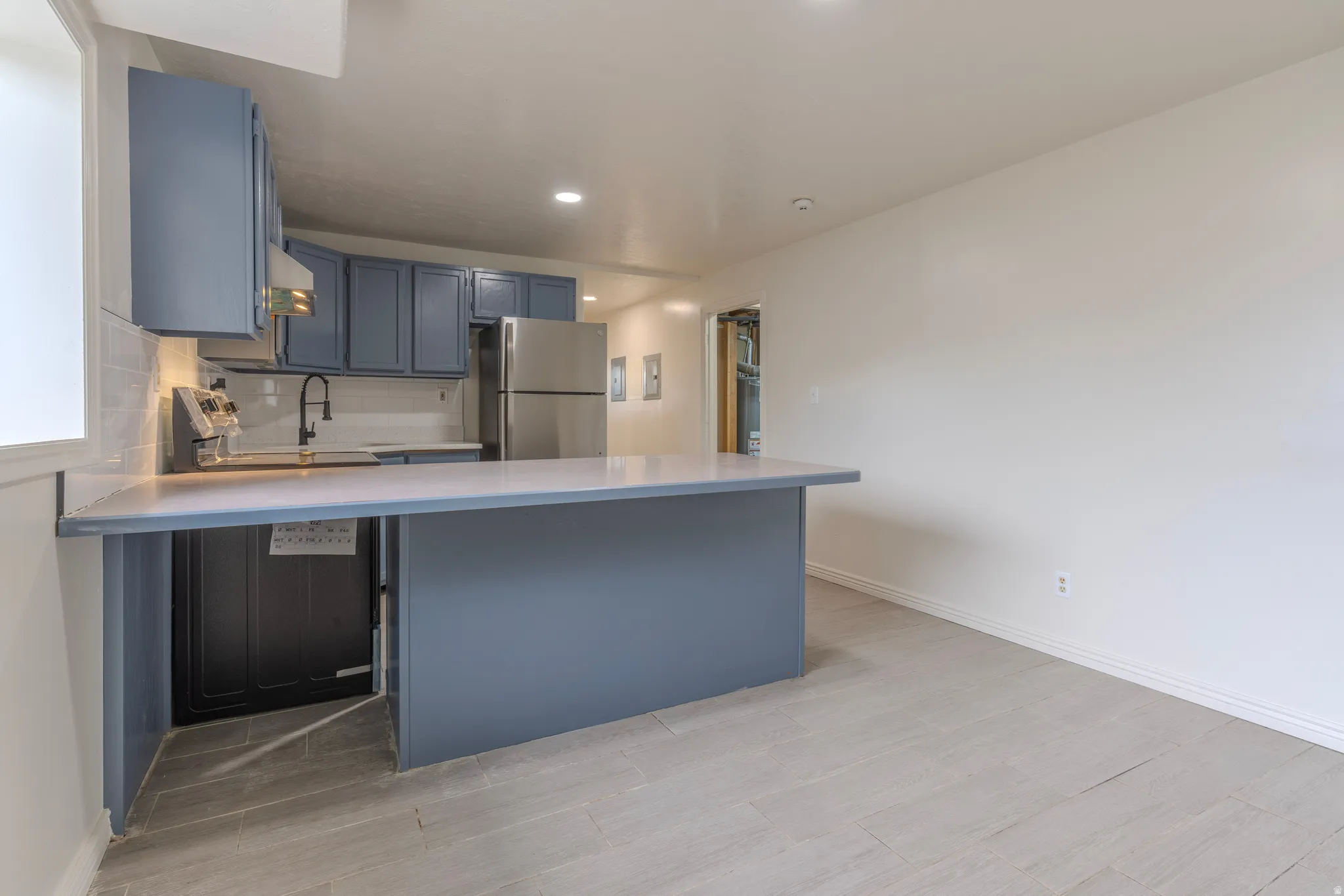 Kitchen with blue cabinetry, stainless steel refrigerator, white subway tile backsplash, and light-toned countertops
