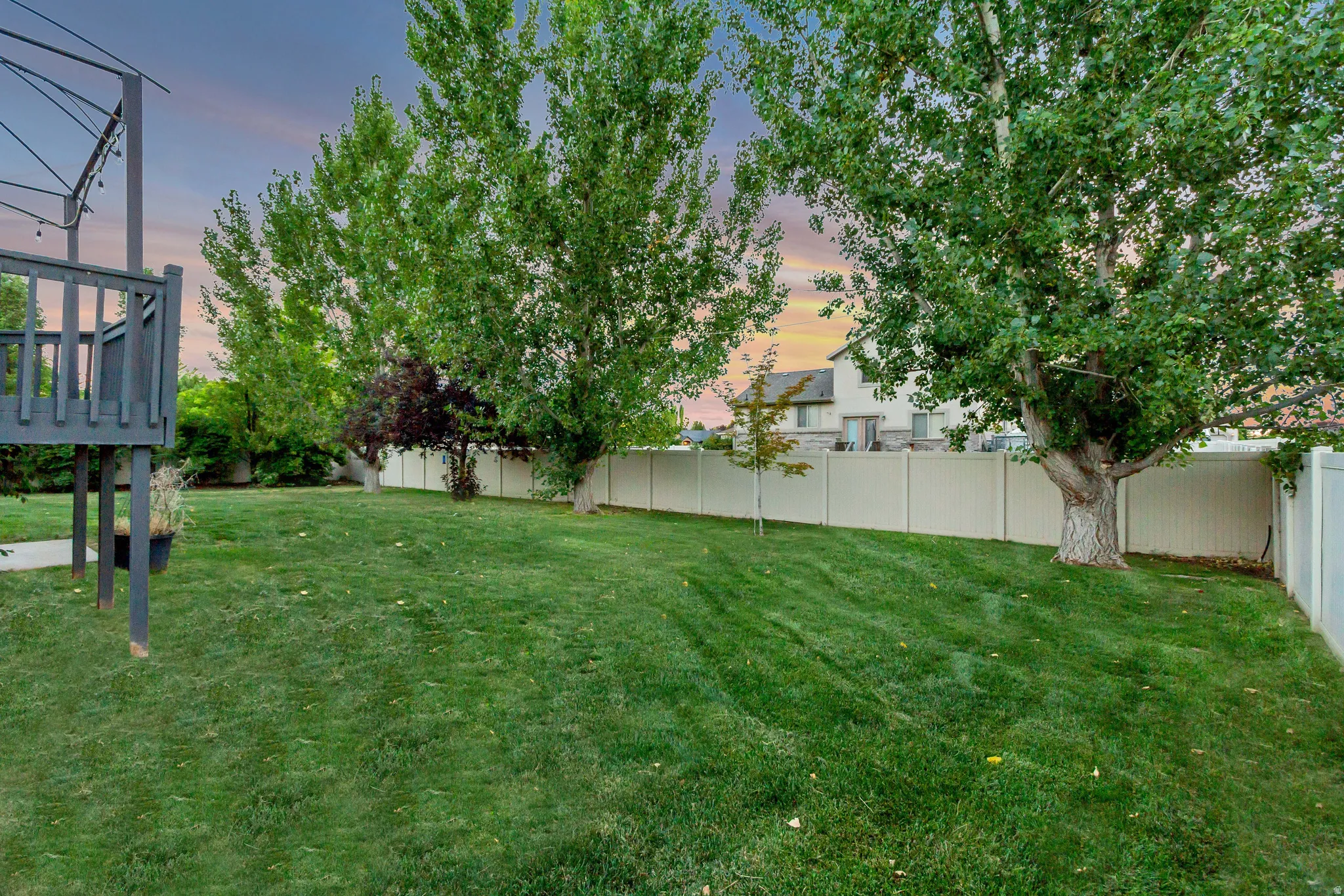 Expansive backyard featuring a manicured lawn, mature trees, and a privacy fence