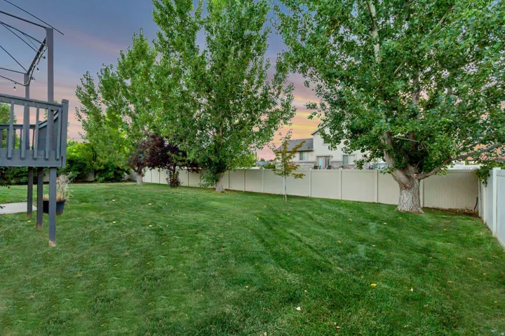 Expansive backyard featuring a manicured lawn, mature trees, and a privacy fence