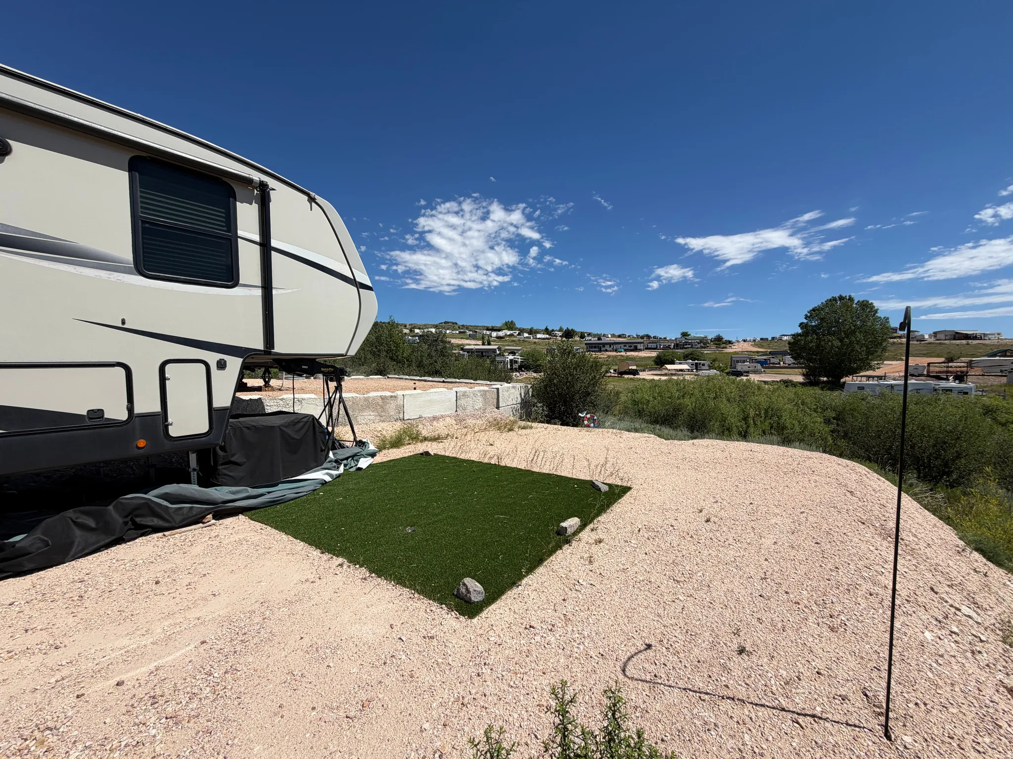 Gravel lot featuring a square of artificial turf and distant structures