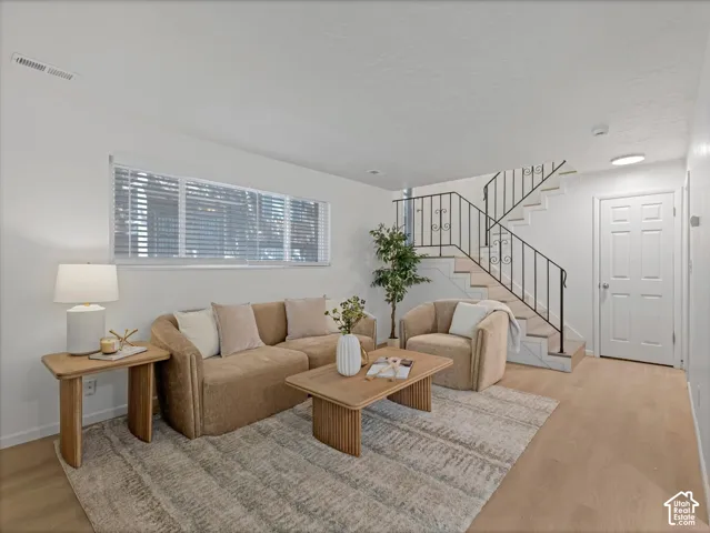 White walls, window with horizontal blinds, light wood-finish flooring, and a staircase with decorative black metal railings