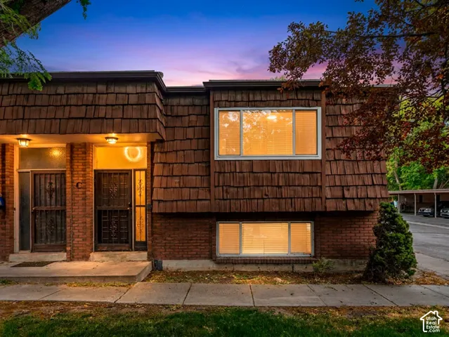 Facade featuring brick and wood shingle-style siding, multiple windows with horizontal blinds, and a concrete walkway