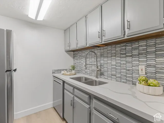Updated kitchen featuring a stainless steel refrigerator, light gray cabinetry with brushed nickel hardware, and a modern tile backsplash