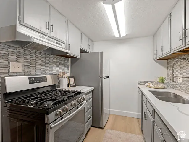 Kitchen featuring stainless steel appliances, stone-look countertops, patterned tile backsplash, and light wood-finish flooring