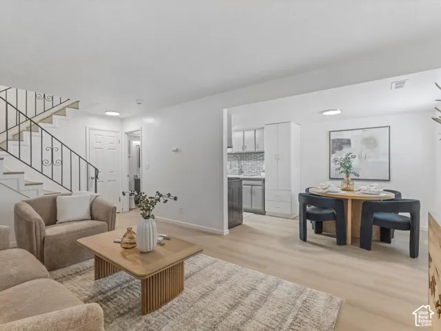 Light wood-finish flooring throughout, stairway with wrought iron railing, white paneled doors, recessed lighting, and a partial view of the kitchen with light cabinetry