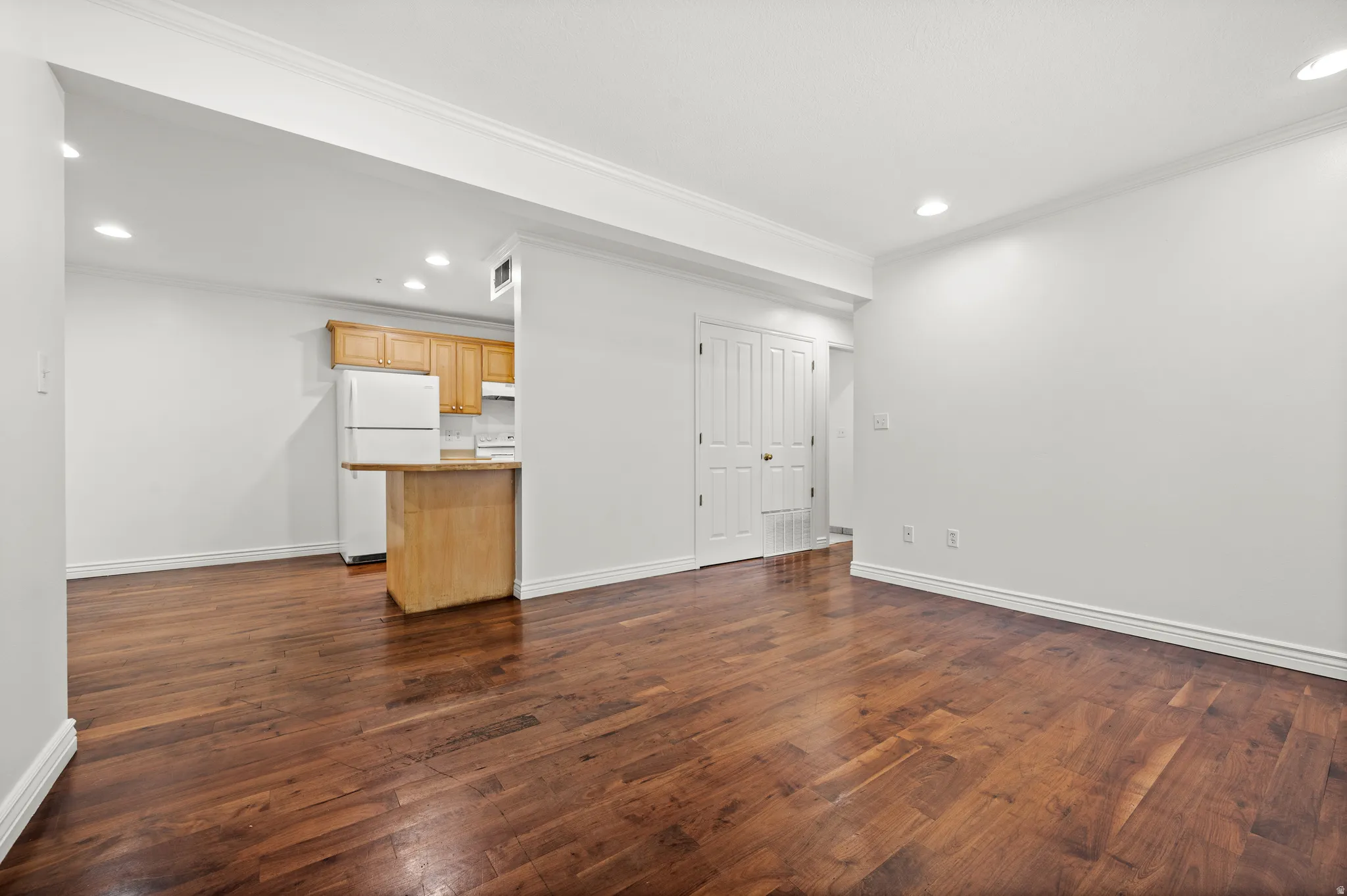 Hardwood flooring, recessed lighting, white walls, white trim, and a kitchen featuring wood cabinetry and a breakfast bar