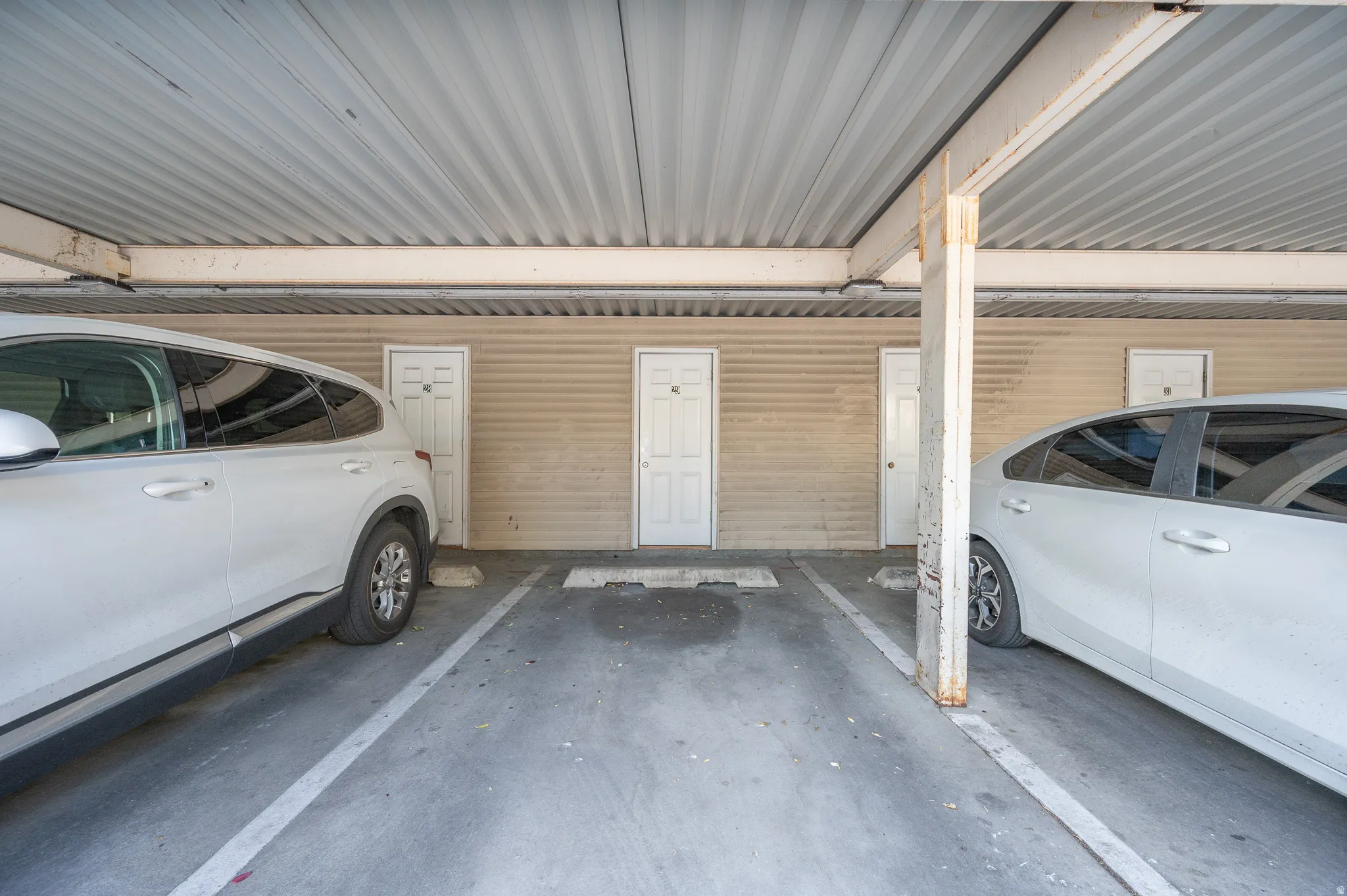 Covered parking area featuring concrete flooring and a corrugated metal ceiling