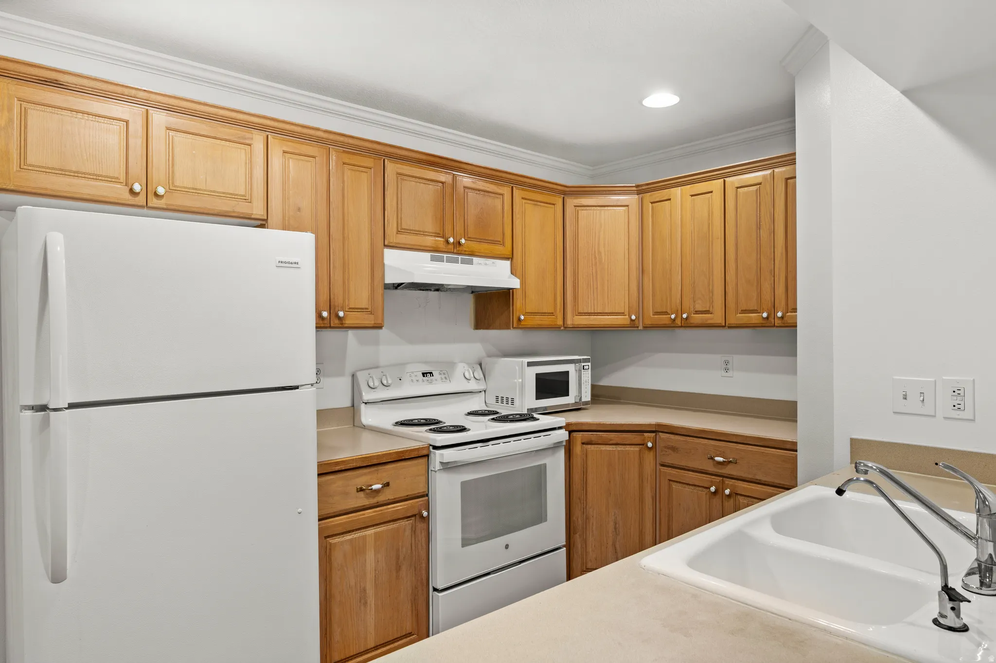 Wood-finish cabinetry, white appliances, and a double basin sink