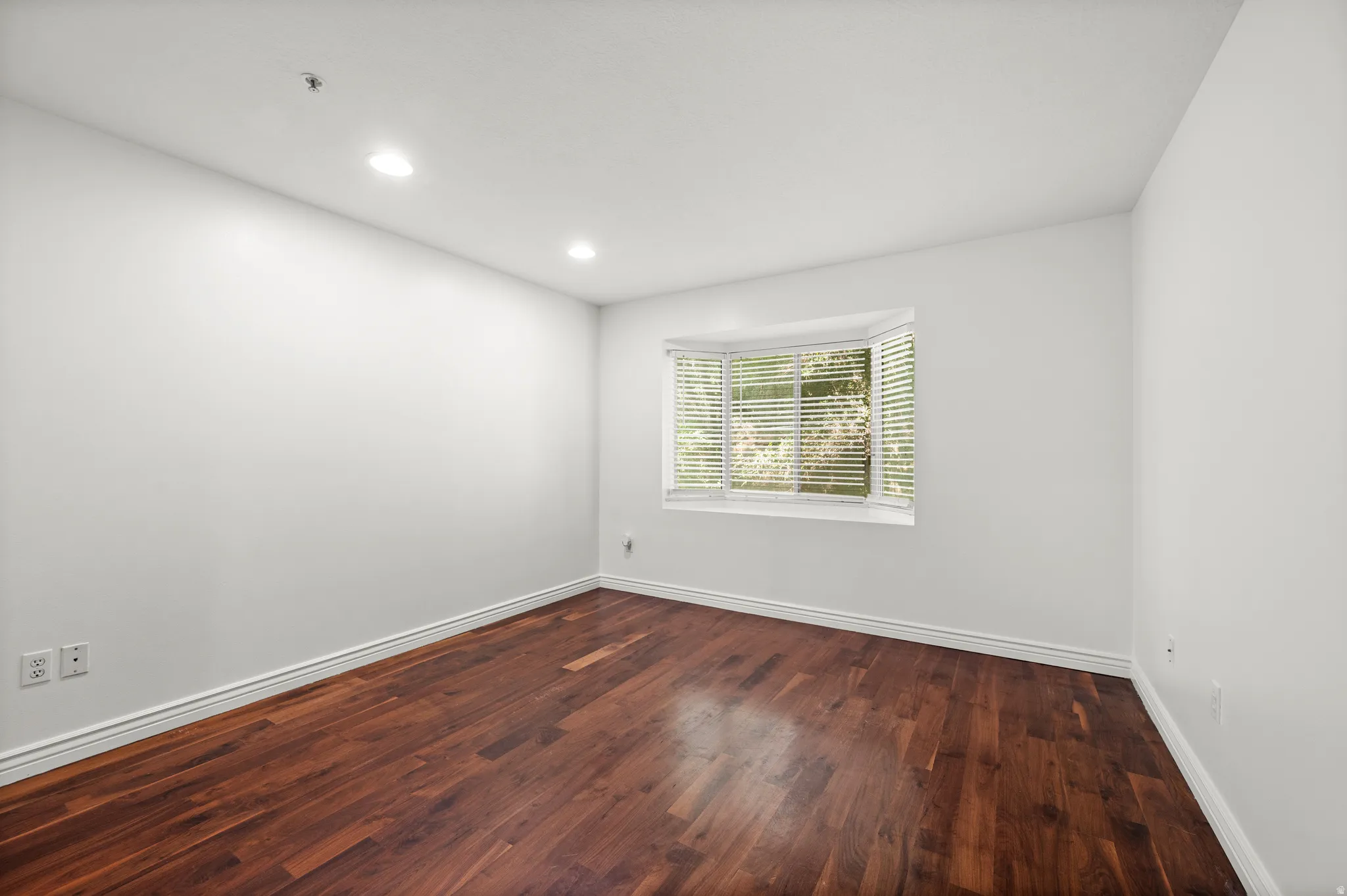 Rich wood-finish flooring, recessed lighting, and a bay window with blinds
