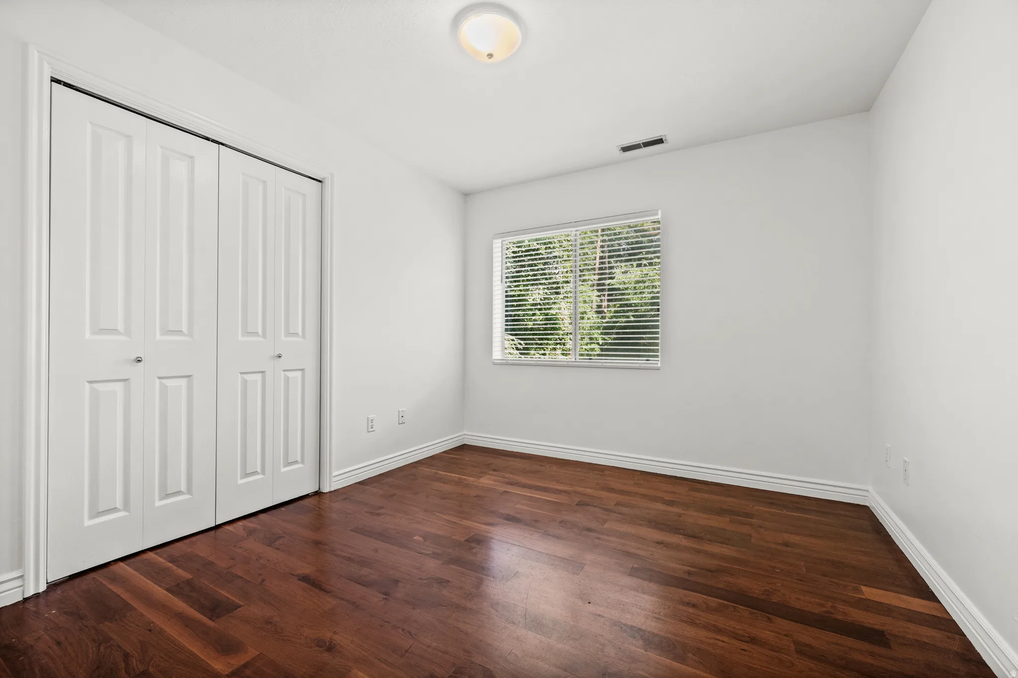 Rich wood-finish flooring, white walls, and a window with horizontal blinds