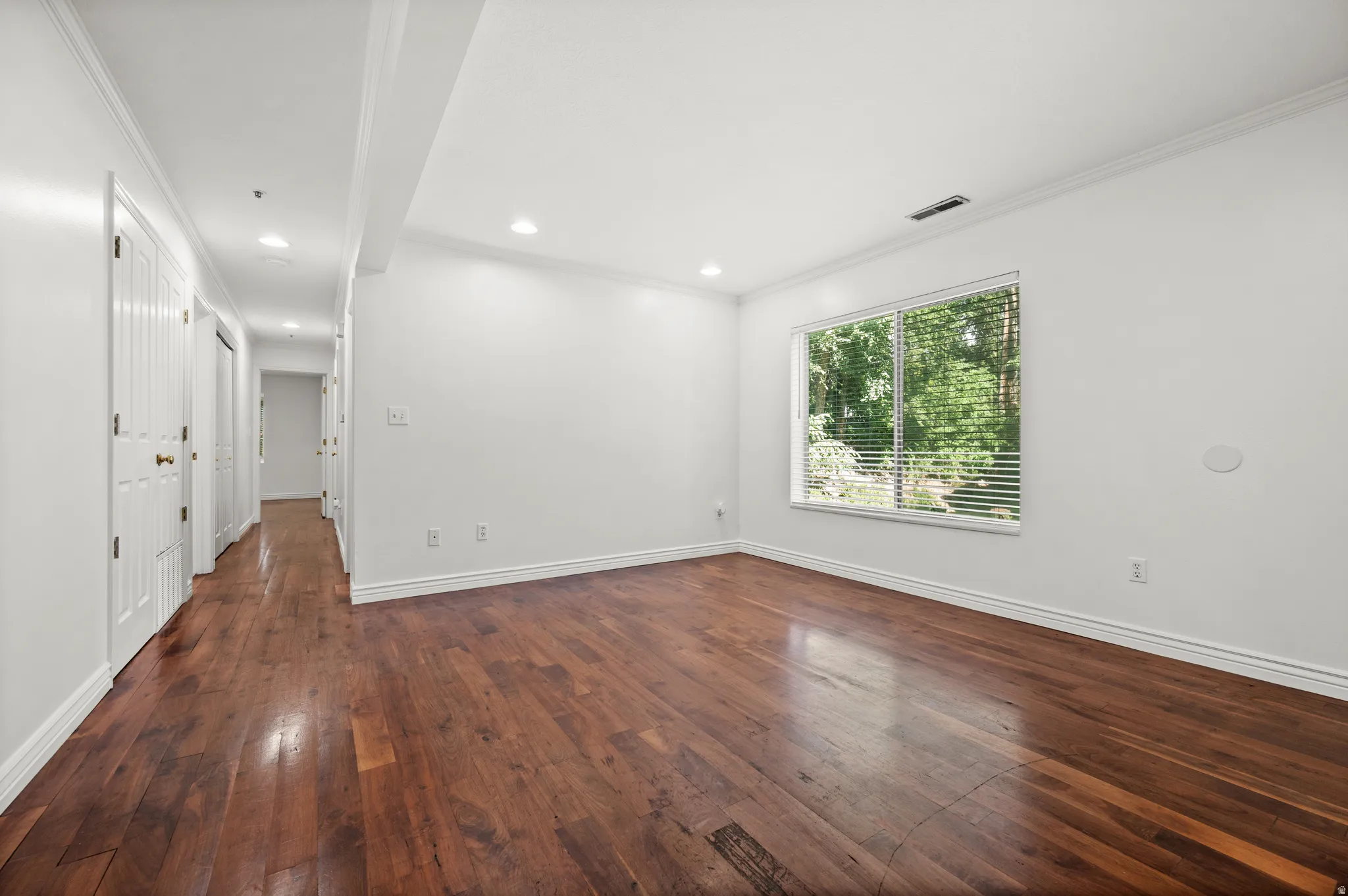 Rich wood-finish flooring, recessed lighting, crown molding, and a spacious window with blinds