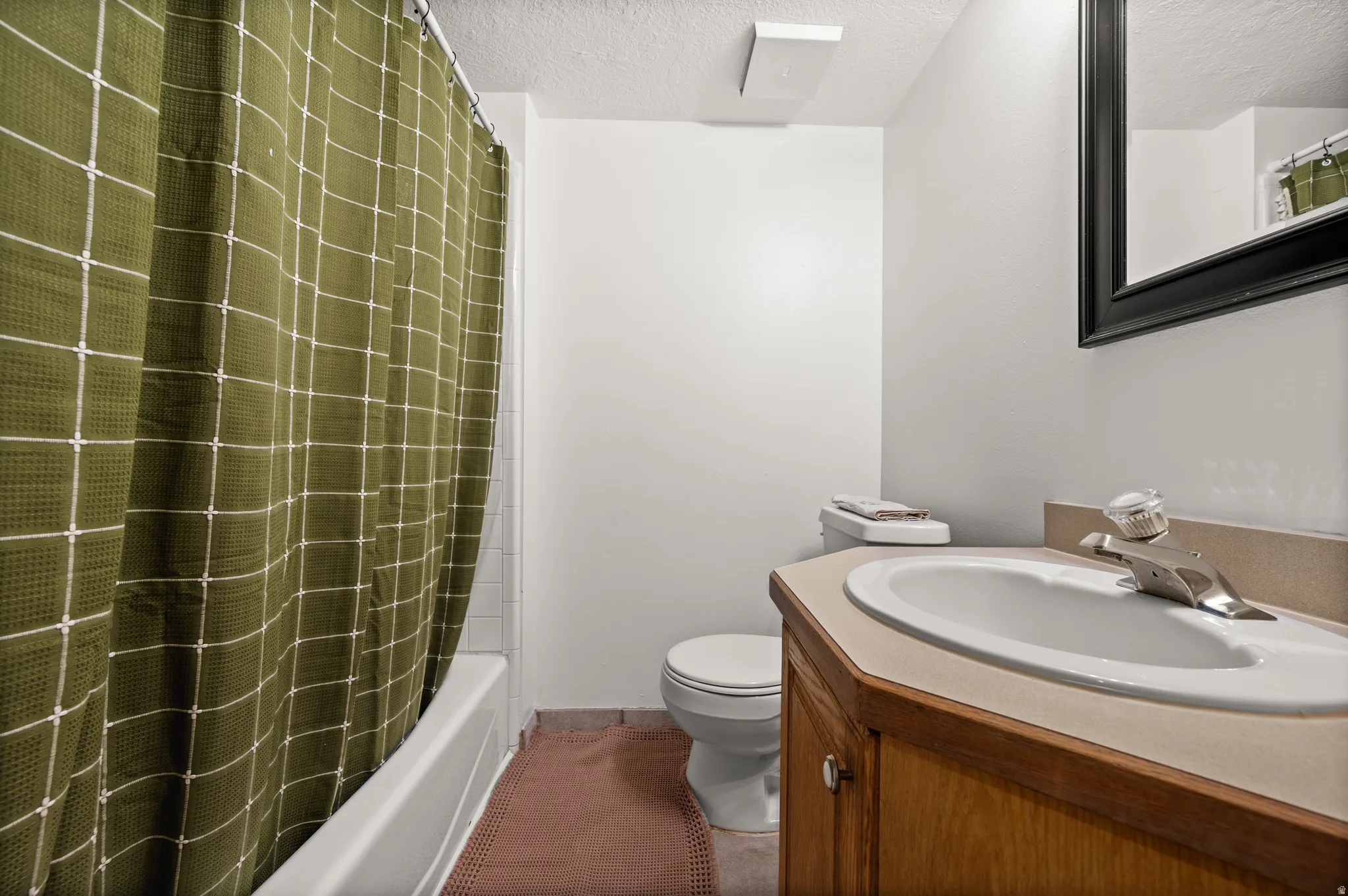White bathtub with tiled surround, wood-finish vanity with an integrated sink and light-toned countertop, and a wall-mounted mirror