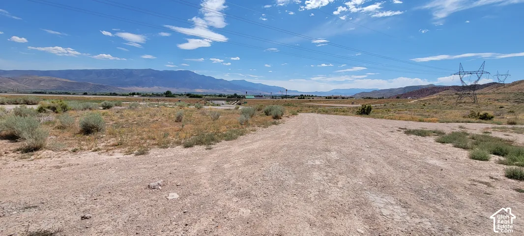 Expansive open land featuring a dirt path, natural scrub brush, and distant mountain ranges