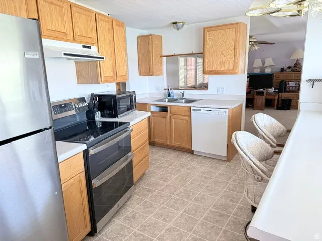 Kitchen featuring wood-finish cabinetry, stainless steel refrigerator, black electric range with double ovens, white dishwasher, and light-toned tile flooring