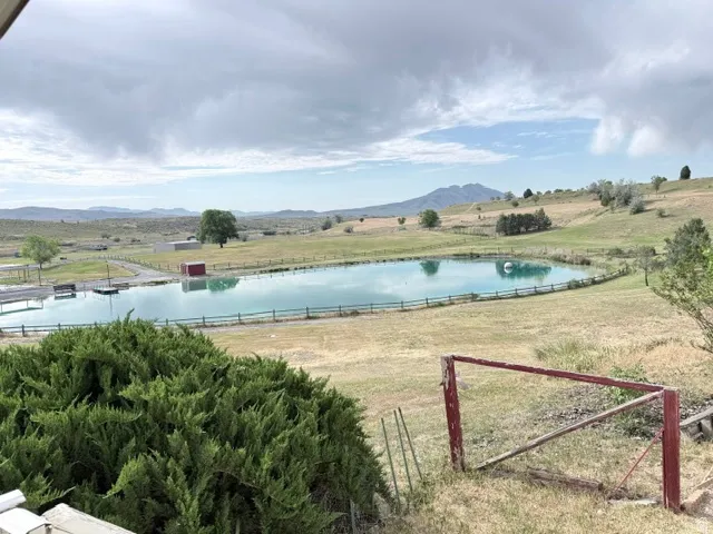 Expansive property featuring a tranquil pond, surrounding green pastures, distant hills, and mature trees