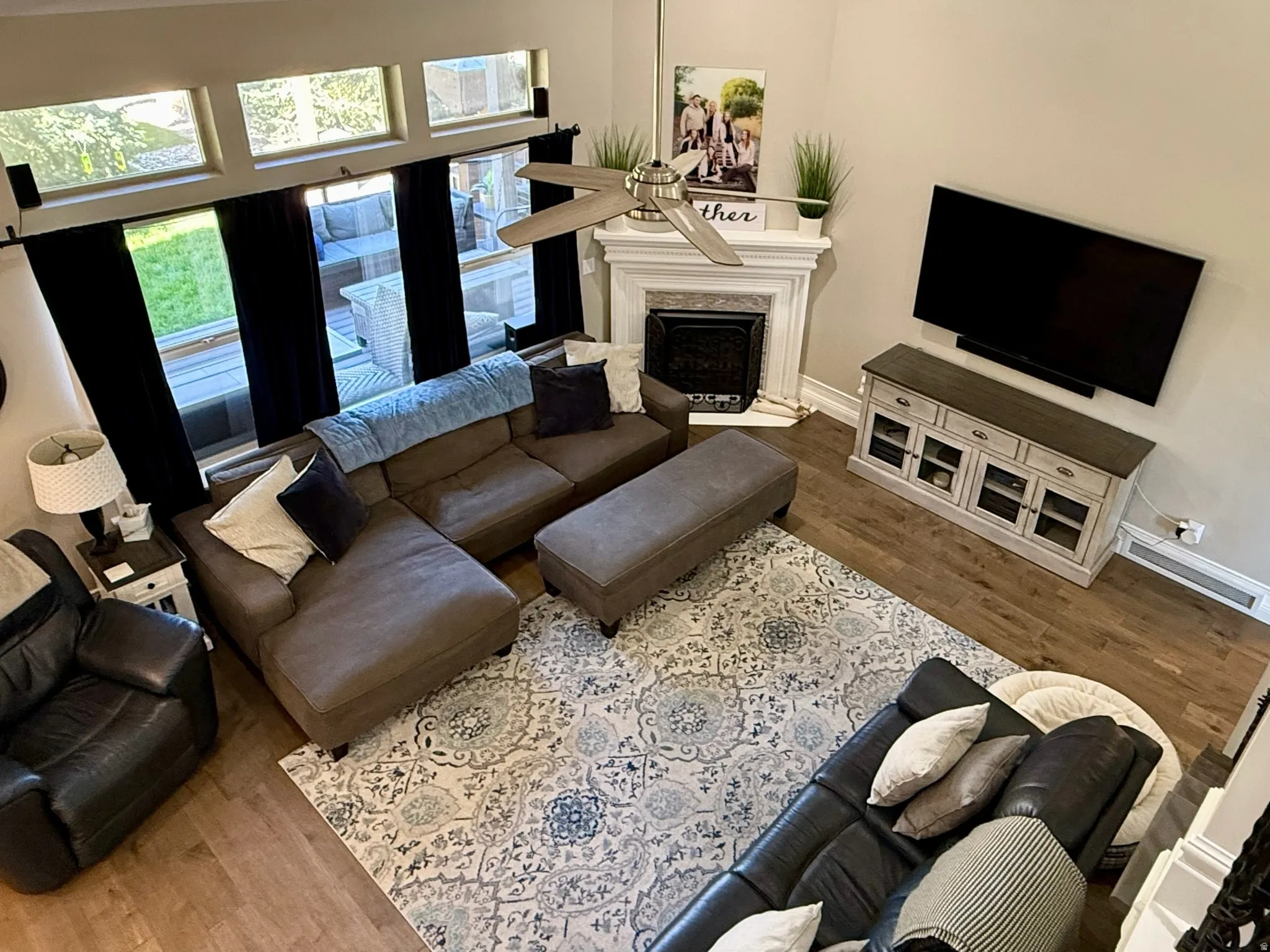 Spacious living area featuring wood-finish flooring, a fireplace with a decorative mantel, and high windows providing natural light