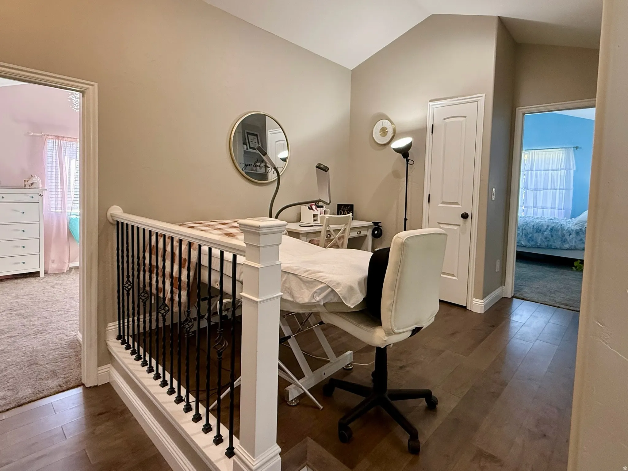 Open loft area featuring wood-finish flooring, a vaulted ceiling, and a white balustrade with black iron spindles